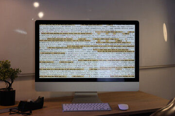 Computer monitor with programming code on desk in office at night