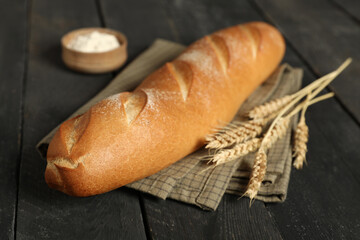 Fresh baguette with wheat and bowl of flour on black wooden background