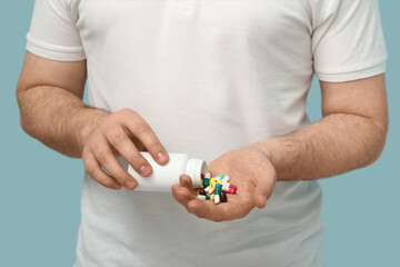 Young man with bottle of different pills on blue background, closeup