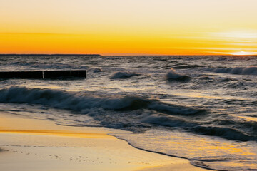 Ocean with waves, sunset sky is orange. water is choppy and waves are crashing on shore. beauty in nature, wild sandy beach at sunset. vacation or travel.