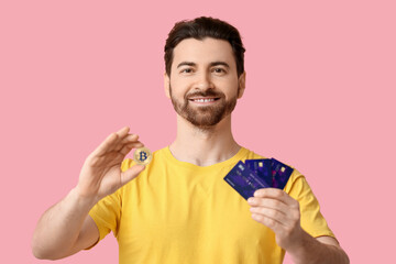 Handsome man with bitcoin and credit cards on pink background