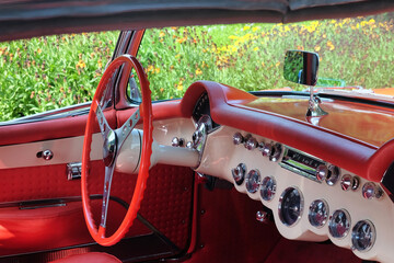American vintage sports car with red leather interior, pink-red steering wheel, and round chrome instruments.