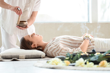 Healer with Tibetan singing bowl cleansing aura of meditating young woman
