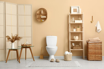 Interior of stylish restroom with ceramic toilet bowl, folding screen and shelving unit