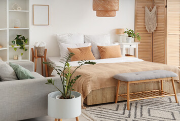 Interior of light bedroom with cozy bed, sofa, folding screen and shelving unit