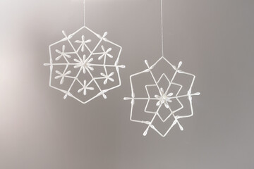 Elegant two white geometric snowflake decorations on light gray background. Delicate winter-themed decor for festive branding, gift wrapping designs, interior design promotions, holiday campaigns