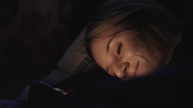 Happy woman is looking at her phone while laying in bed. She is sad or upset