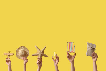 Female hands holding mini deck chairs with starfish, hat and plane on yellow background
