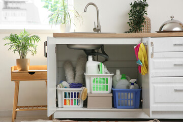 Baskets with different cleaning supplies under sink in kitchen