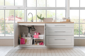 Baskets with different cleaning supplies and paper towels under sink in kitchen