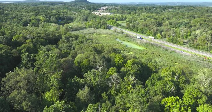 Daytime aerial video over a stretch of interstate, highway, through a green vegetative area. 