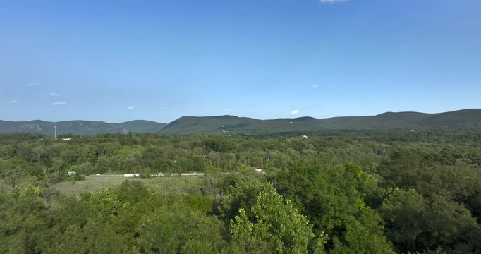 Daytime aerial video over a stretch of interstate, highway, through a green vegetative area. 