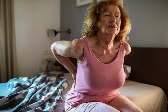 Senior woman waking up with back pain in the morning at home