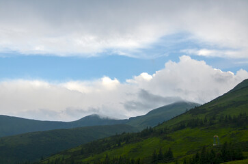 Serene mountain scenery featuring layered hills shrouded in clouds under a bright blue sky. A tranquil atmosphere of natural beauty and calmness, perfect for themes of escape and nature's serenity