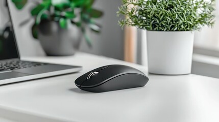 Modern minimalist wireless mouse on a white desk, alongside a laptop and plants