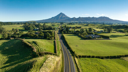 The volcanic cone of Mt Egmont in the distance driving down a rural country road through agricultural fields