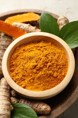 Aromatic turmeric powder in bowl, fresh roots and leaves on light grey table, closeup