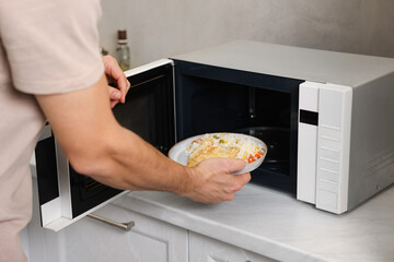 Man putting plate with lunch into microwave in kitchen, closeup