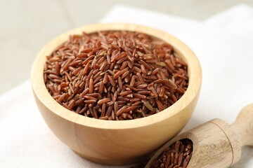 Brown rice in bowl and scoop on table, closeup