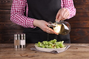 Woman pouring oil onto tasty salad at wooden table, closeup