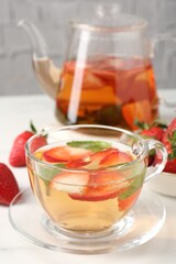 Aromatic fruit tea with strawberries and mint on white table, closeup