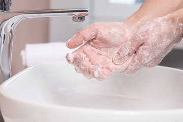 Woman washing her hands with foaming soap above sink in bathroom, closeup
