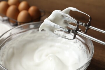 Hand mixer with whisks and bowl of whipped cream on table, closeup