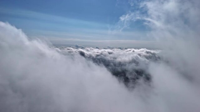 High-altitude drone captures thick white clouds with a view toward the horizon and deep blue sky