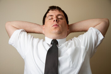 A man in a white shirt and black tie is relaxing with his arms behind his back