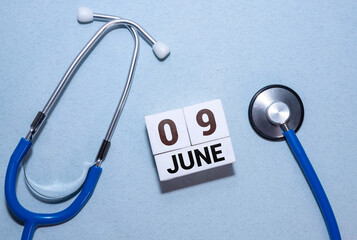Wooden block calendar with date June 9 on pink concrete background.
