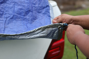Close up hand A man ties a tie-down cord on a car trailer tarpaulin. Cargo transportation.Binding the bundle of rope to the end of the pickup truck. © Jumain