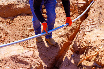 Construction worker lays electrical pipe in filled trench during foundation work