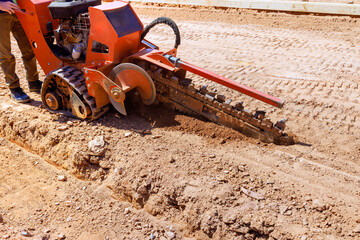 Worker uses trencher to dig seam for underground utilities at construction site.