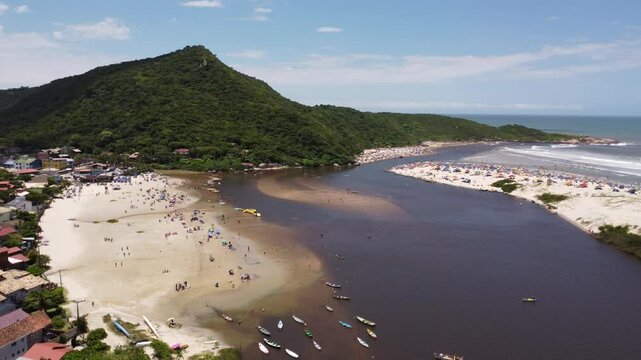 4K drone side tracking of river meeting the sea with beach sports in Guarda do Emba&uacute;, Brazil