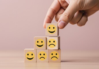 A hand places a smiley block atop a wooden stack, representing positive emotion and satisfaction.