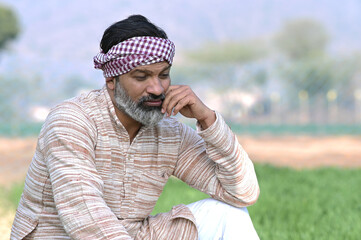 Indian sad and discouraged farmer man sitting in crop farmland and lost deeply his agriculture...