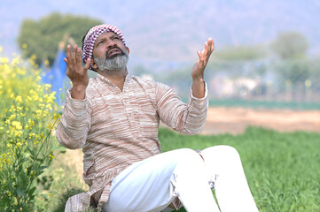 Indian sad and discouraged farmer man sitting in crop farmland and lost deeply his agriculture...