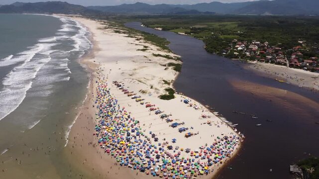 4K drone beach shot over river and ocean at Guarda do Emba&uacute; with tourists and boats &ndash; Brazil