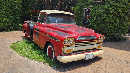 Red vintage truck parked on road beside traffic light with tree and house or home background. Retro or classic vehicle and old car style for show.