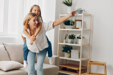 Mother joyfully lifting daughter on shoulders in cozy living room with warm natural light and...