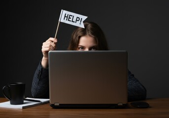 A businesswoman seeks help while working on her laptop in a dark office environment.