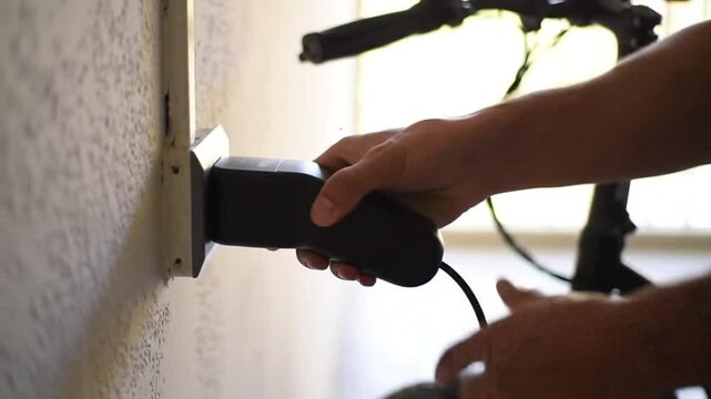 Person plugging in electric bicycle charger into wall outlet close up