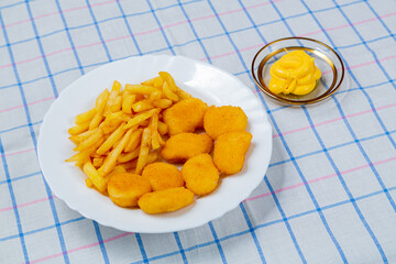 French fries and crispy nuggets in a plate on a white checkered tablecloth