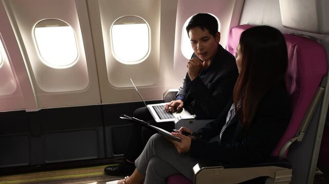 businessman and his secretary discuss sales paper while traveling by plane to sign a contract with another company, during the business trop of the two businessmen they double-checked to be sure
