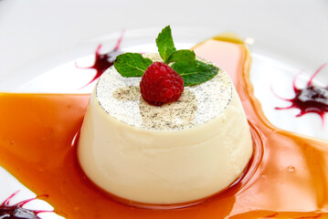 Panna cotta with caramel sauce and red berries, garnished with raspberries and mint leaves. Sweet food.