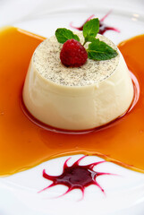 Panna cotta with caramel sauce and red berries, garnished with raspberries and mint leaves. Sweet...