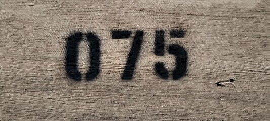 The number 075 is spray painted with black spray paint on wood