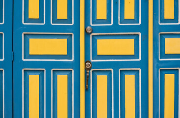 Puerta colonial azul y amarilla con diseño geométrico en madera pintada, detalle arquitectónico...