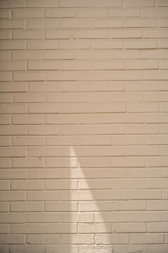 Pared de ladrillo pintada de color crema con sombra triangular proyectada por la luz del sol