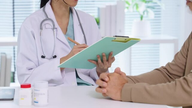 Doctor Reviewing Medical File While Interviewing Elderly Patient at Clinic or Hospital